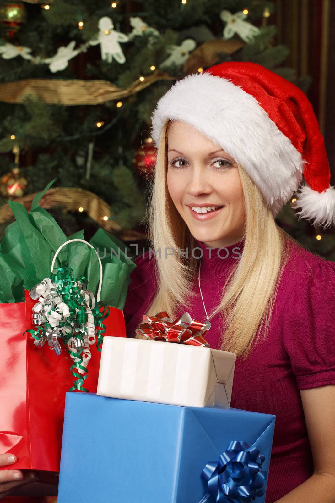 Photo of a beautiful blond female sitting in front of a Christmas tree holding presents.