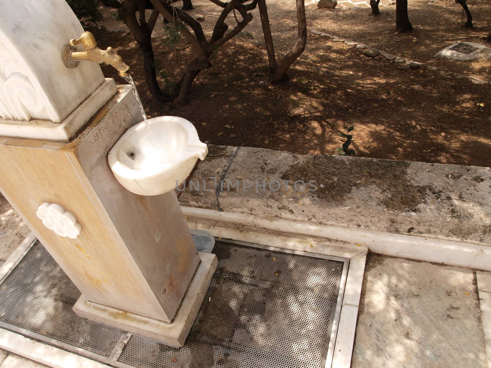 Old marble water faucet with running stream near Acropolis