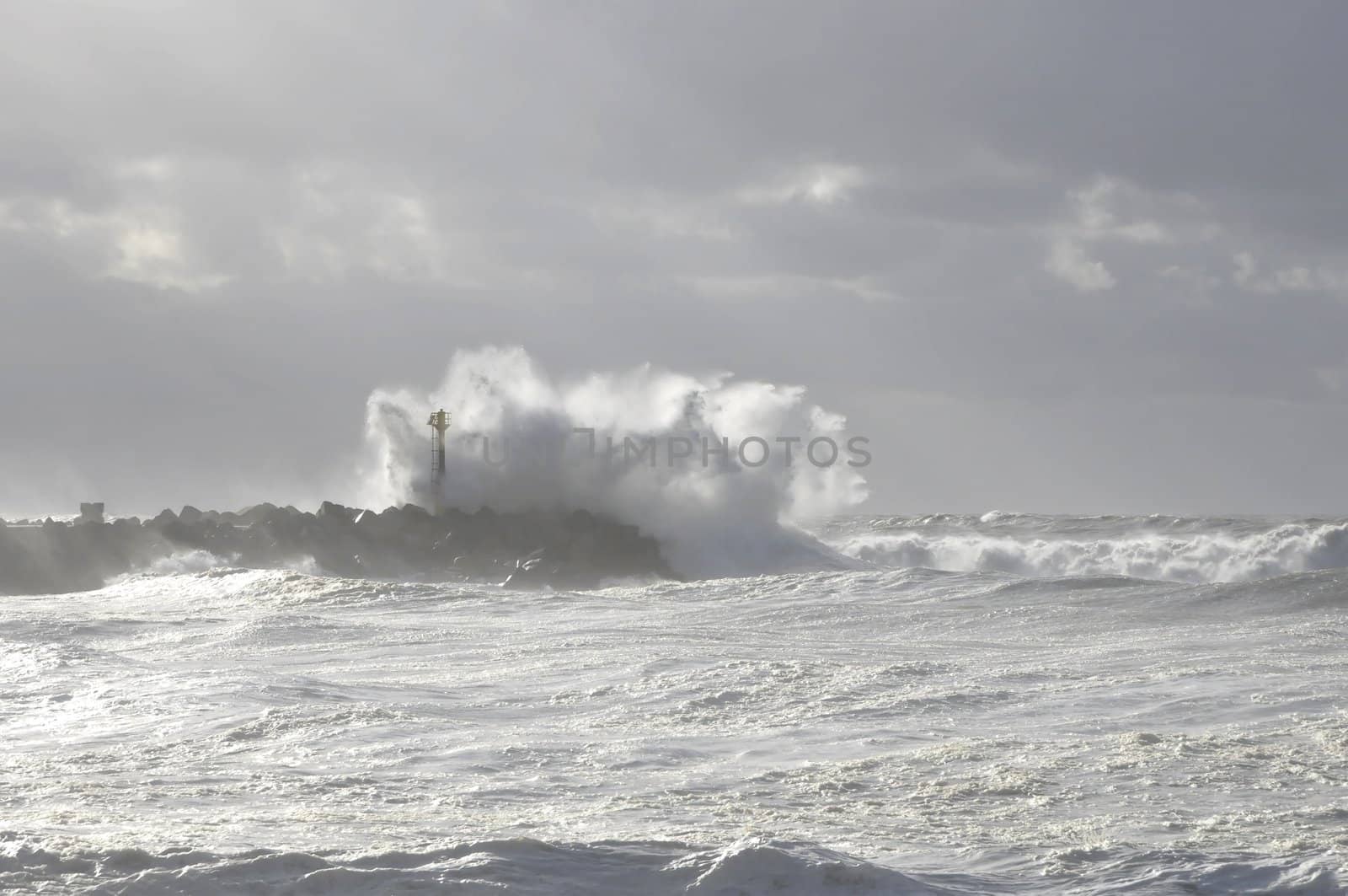 Very big wave on a blocks jetty with a beacon during a storm