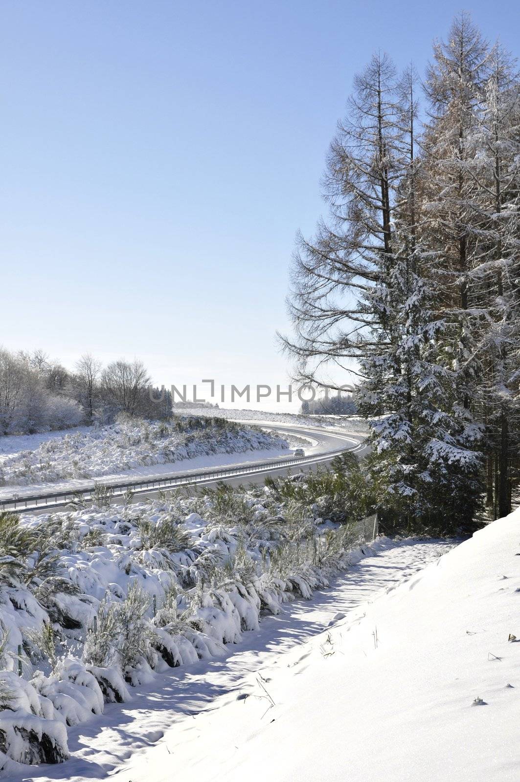 Winter landscape with a blue sky and lot of snow and also a motorway with one car