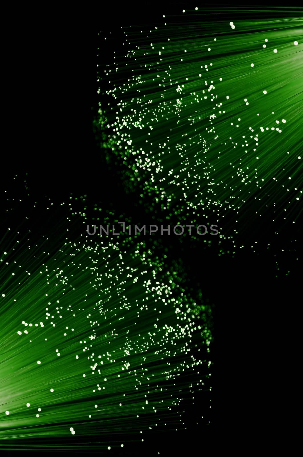 Close up capturing the ends of many illuminated green fibre optic light strands arranged against black.