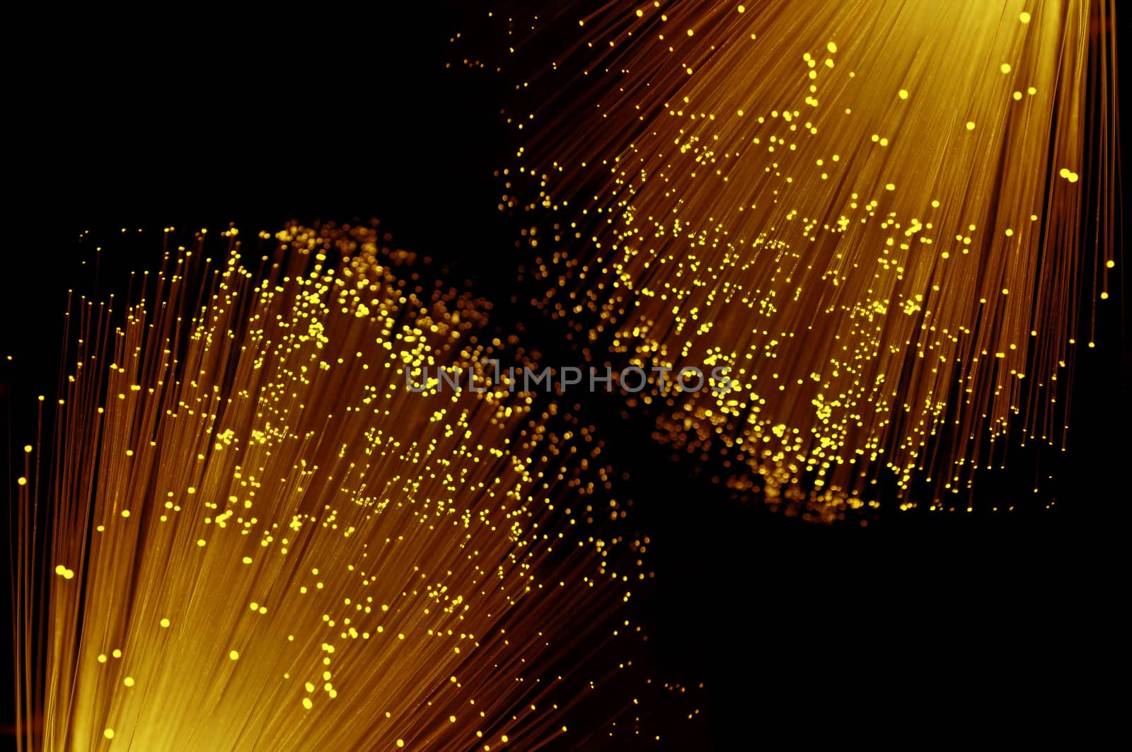 Close up capturing the ends of many illuminated orange, red and yellow coloured fibre optic light strands against a black background.