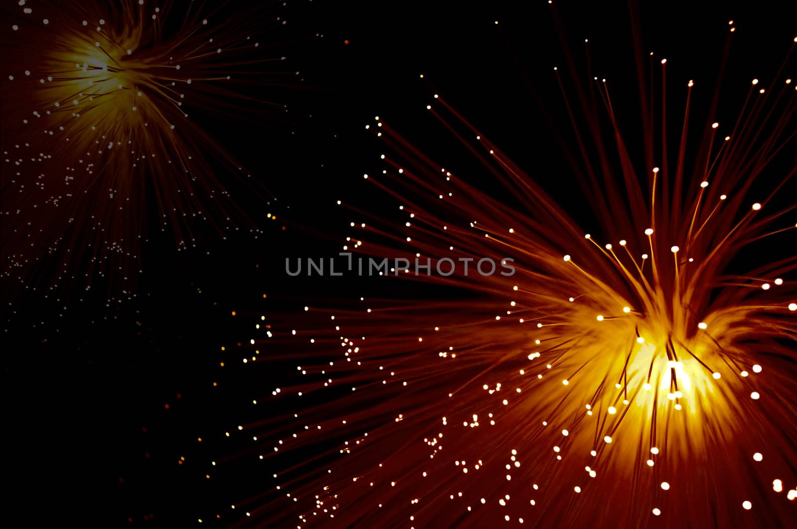 Close up capturing two vibrant orange and red coloured fibre optic lamps illuminated against a black background.