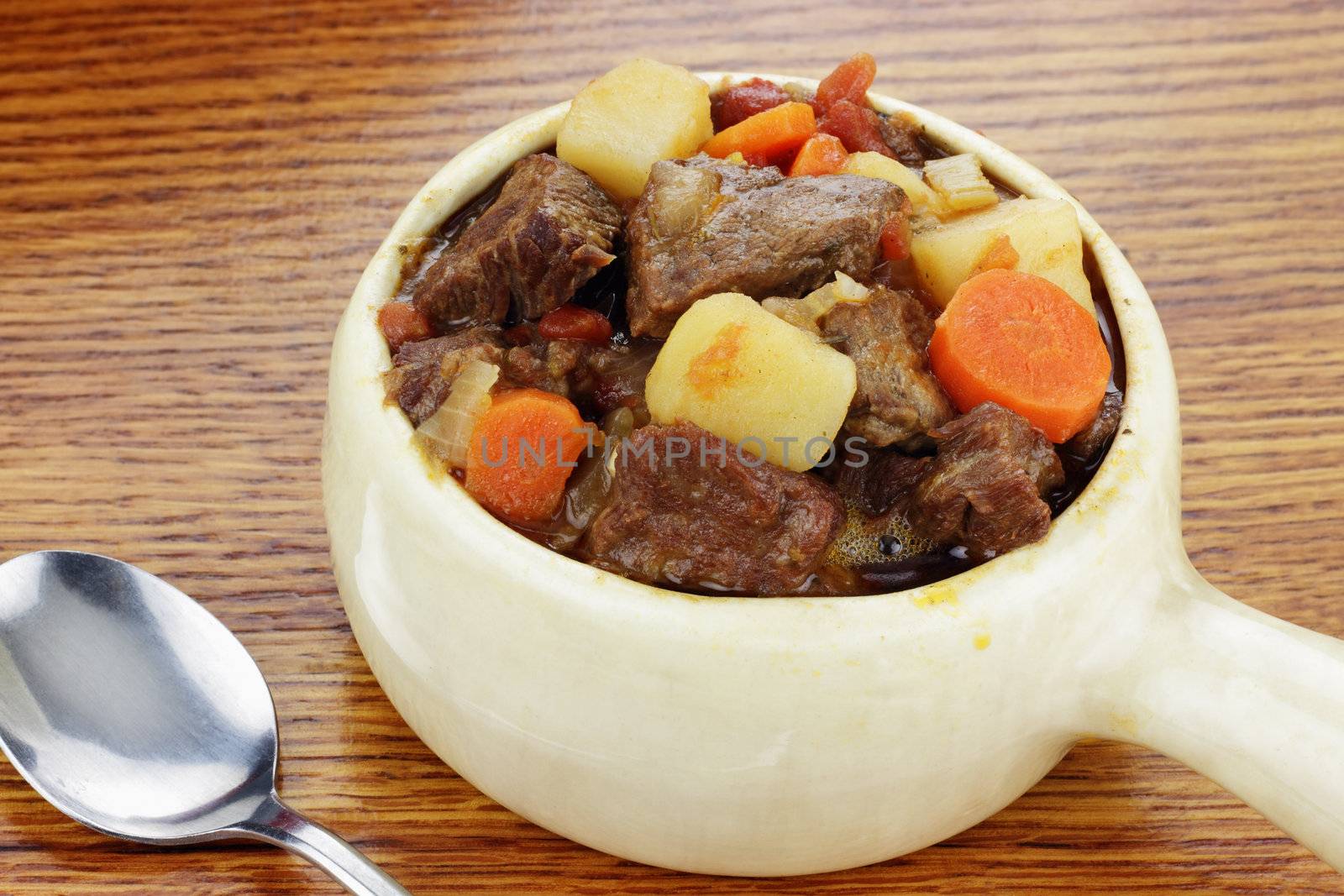 Delicious beef stew served in an onion soup crock with spoon.