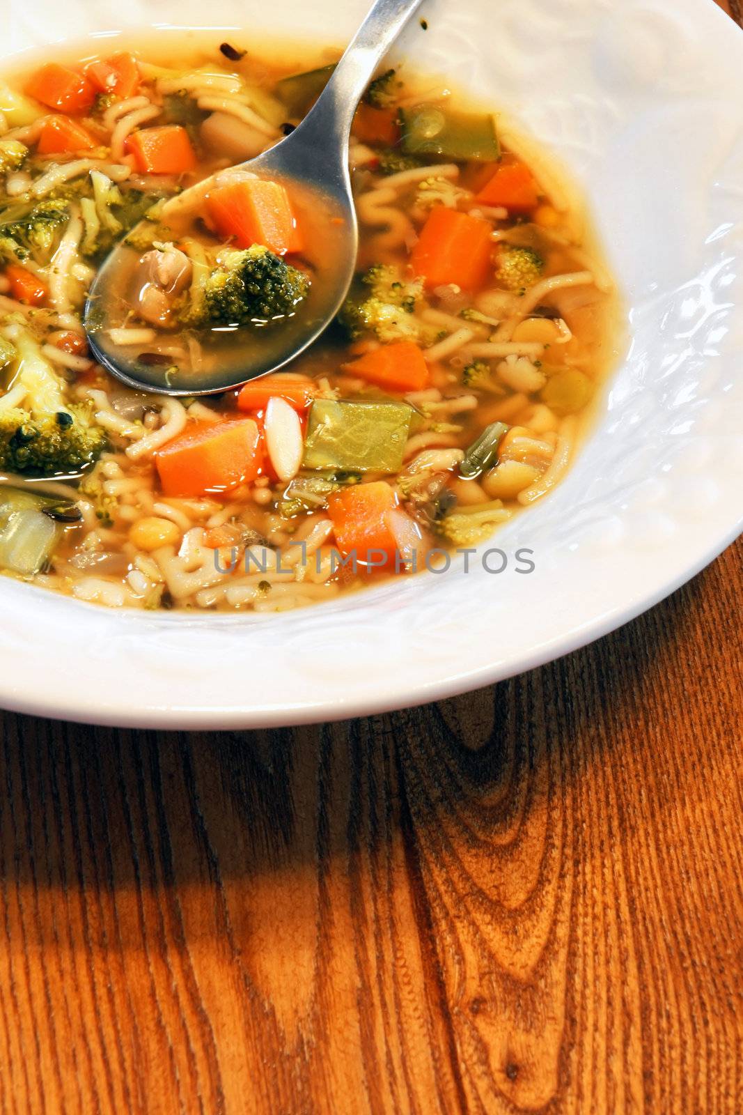 Good hearty homemade vegetable soup served in textured white bowl on wooden kitchen table.