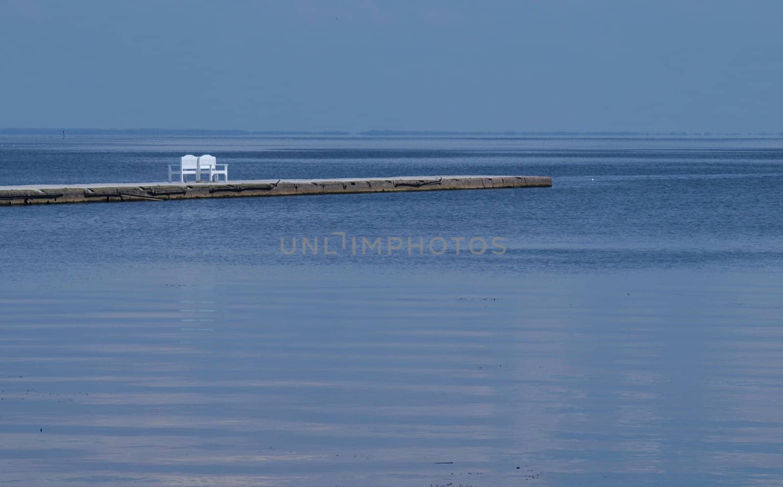 white bench on a pier amidst blue calm water