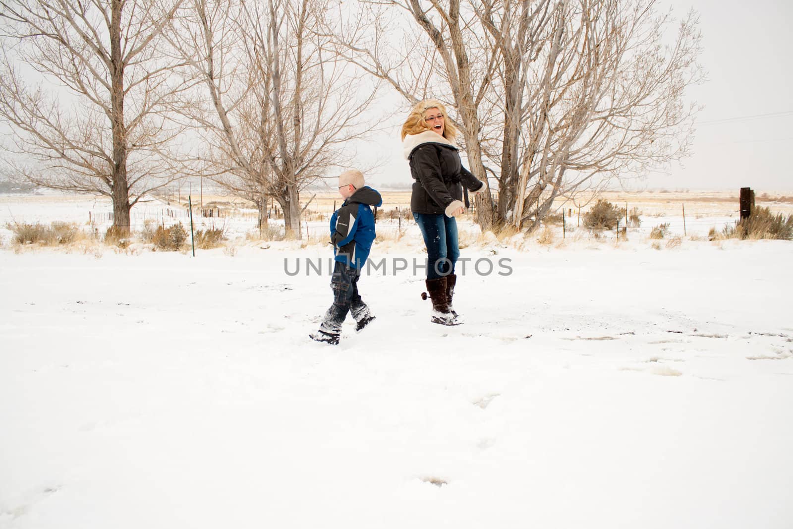 A mother and son jumping in the snow, playing and having fun.