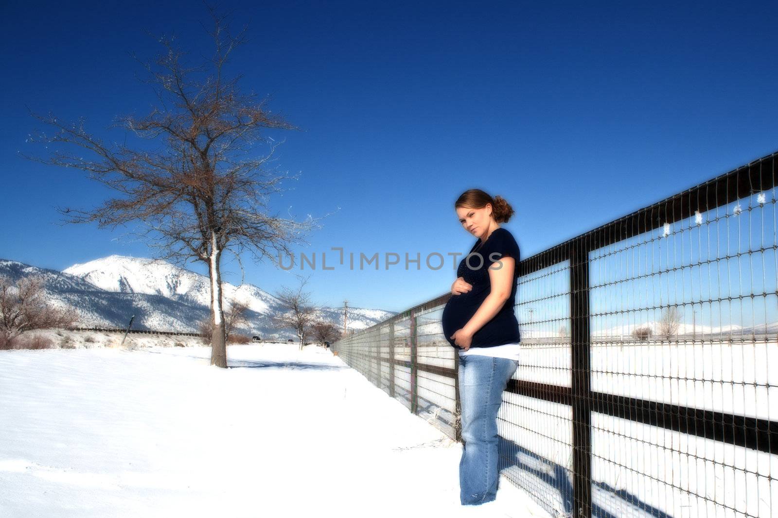 A pregnant girl standing in front of a vanishing fence.