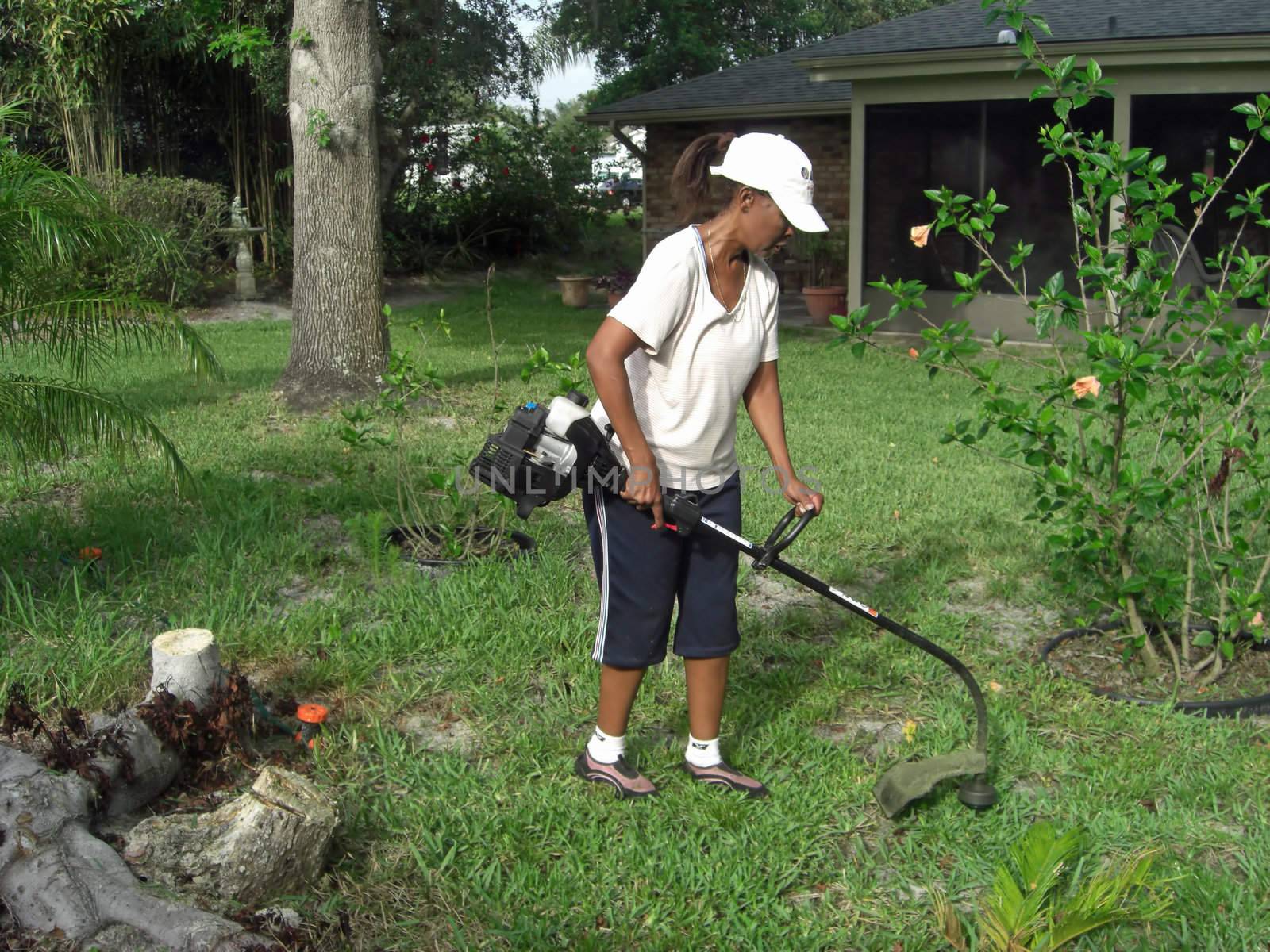 To make ends meet, a woman with a lawn mowing services is trimming the grass with a weed wacker.