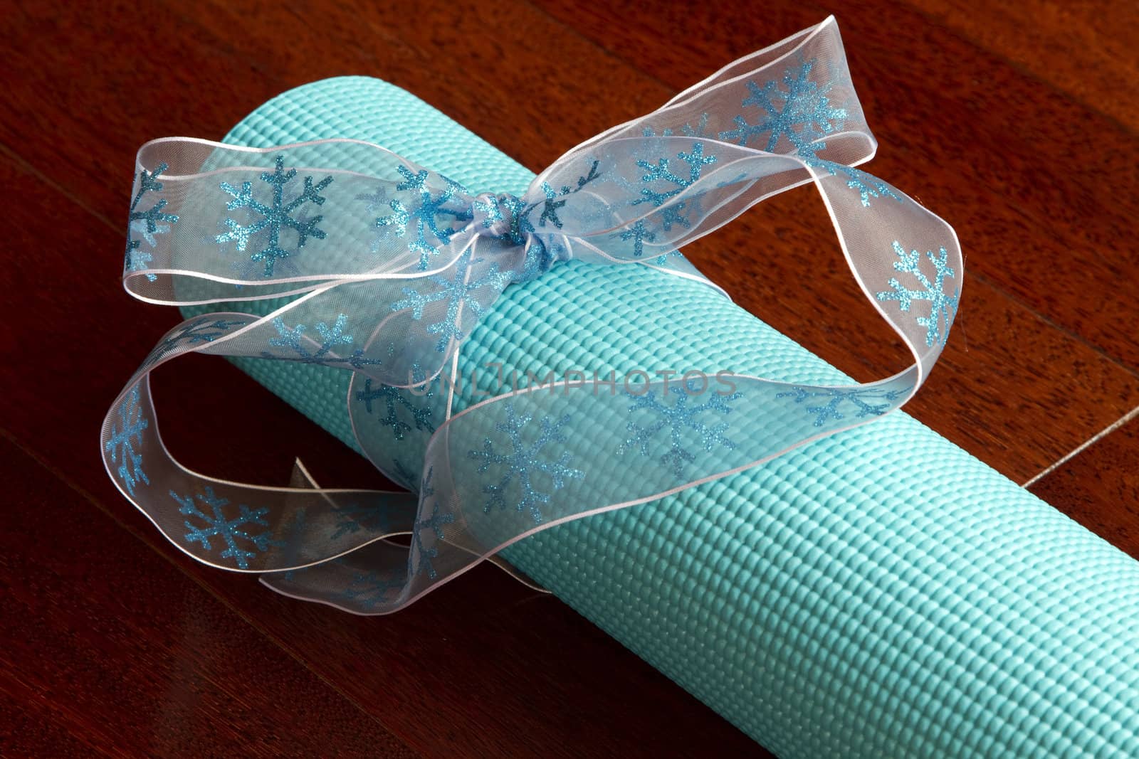 Sky blue yoga mat with blue ribbon is a gift placed on a wood floor