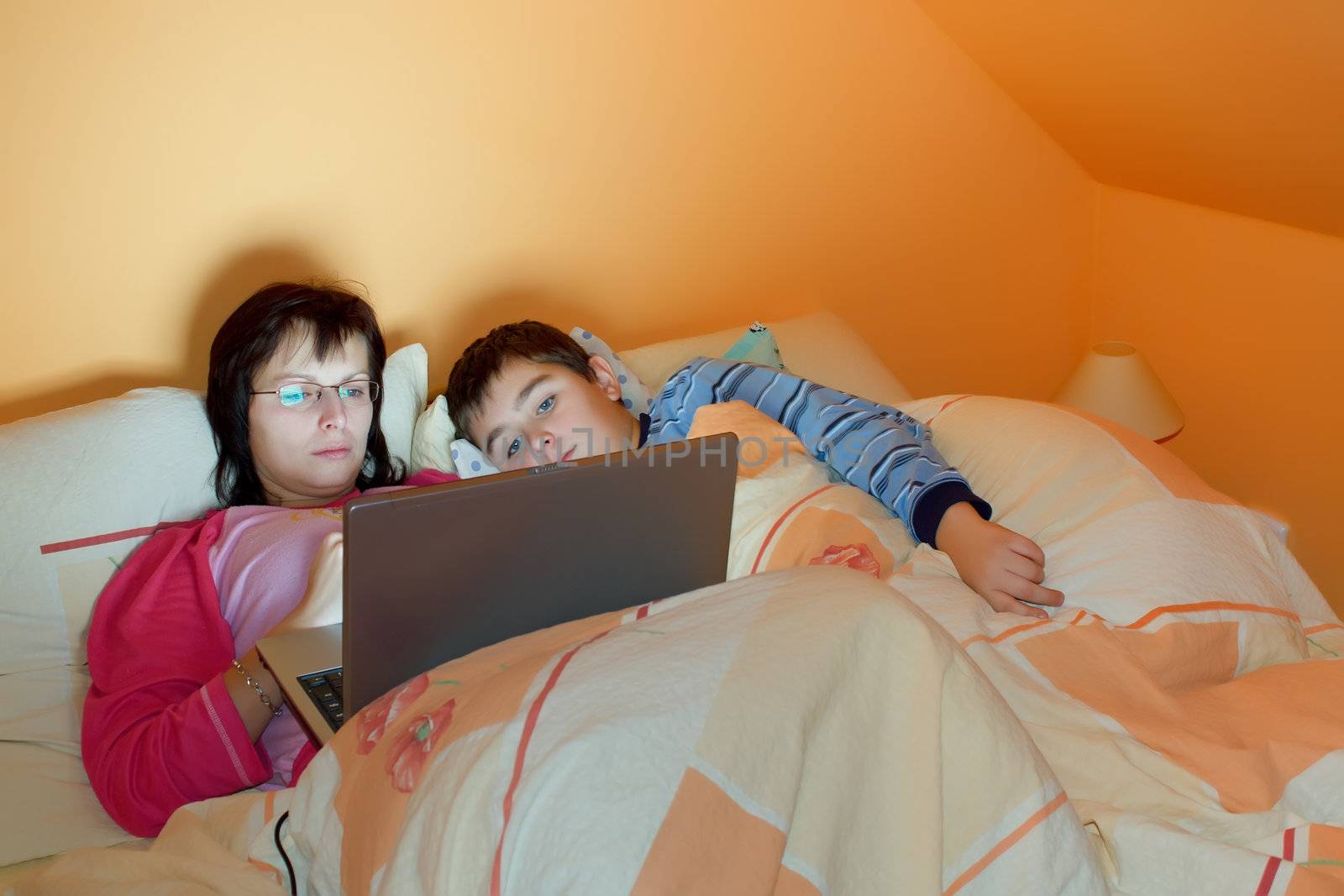 Portrait of a mother and her son using laptop while lying on the bed at home  by artush
