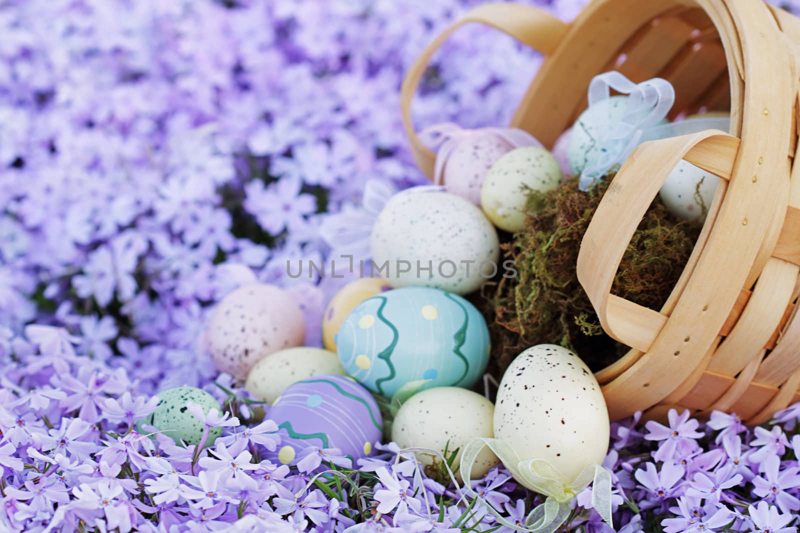 Easter eggs spilling from a basket into a bed of spring flowers. Selective focus on lower portion of image with extreme shallow DOF.