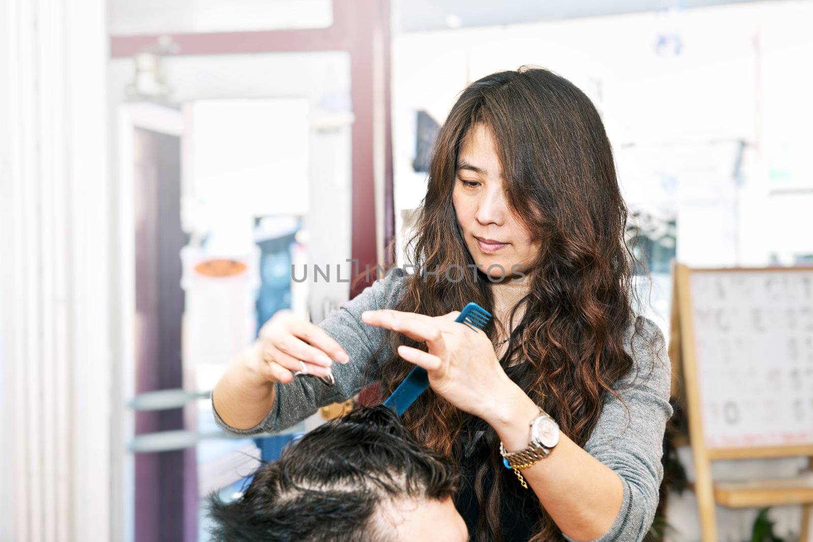 Happy hairdresser cutting hair in her salon