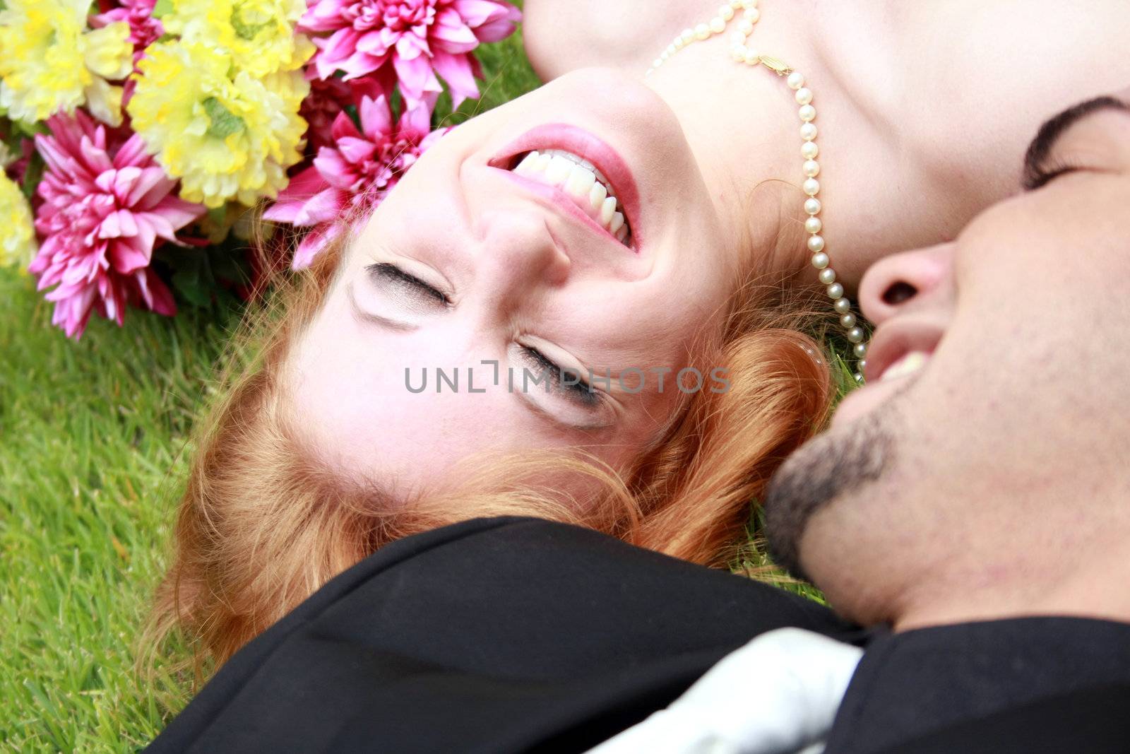 A bride and a groom lying on the grass, smiling