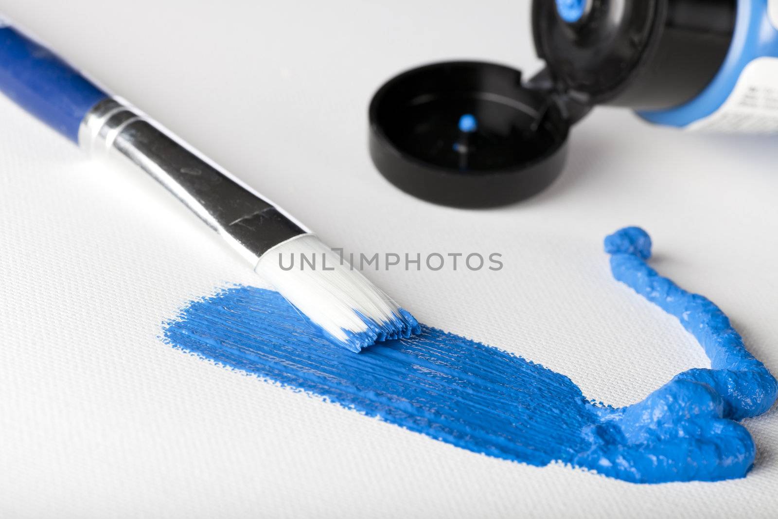 Blue acrylic paint with paint brush and tube of paint in the background