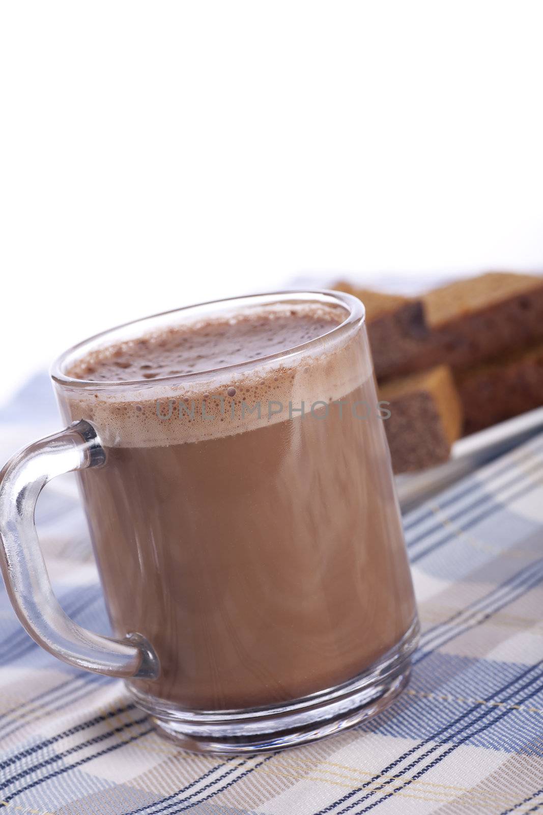 Fresh hot chocolate in glass mug with cake in background.