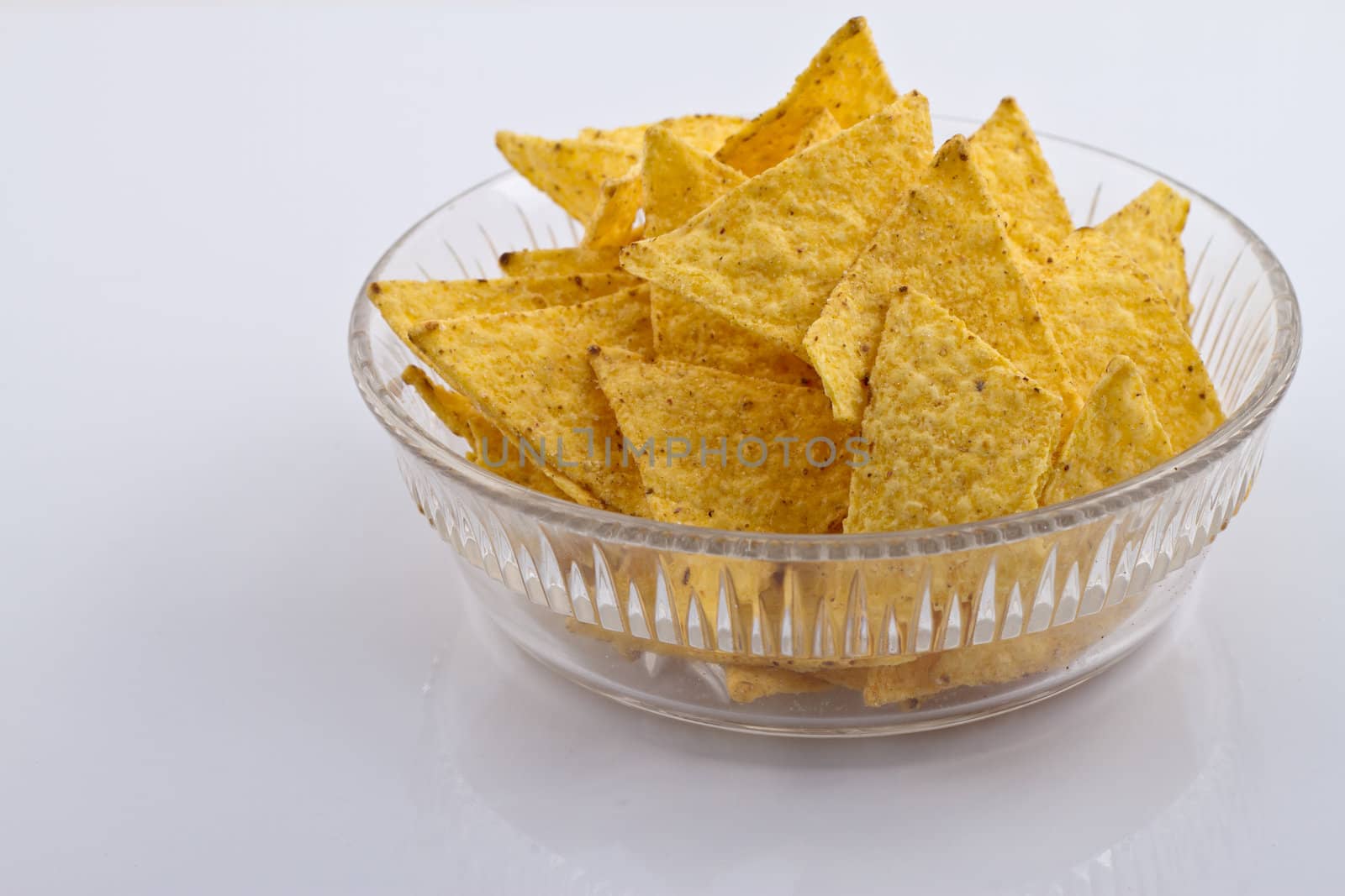 Glass bowl of nachos on white reflecting surface