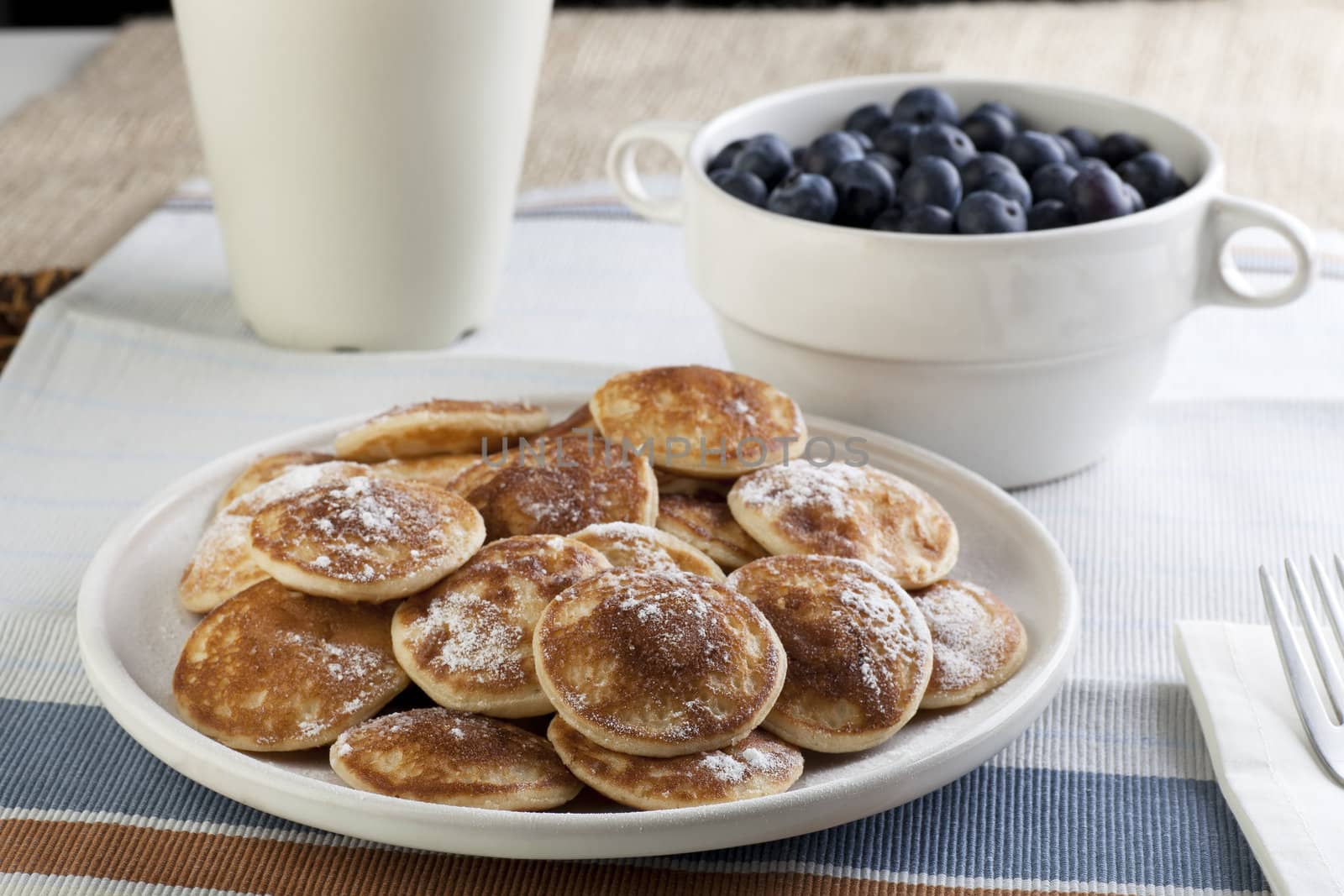 Dutch mini pancakes, or poffertjes, with butter, syrup and powdered sugar.  Fresh blueberries out of focus in the background.