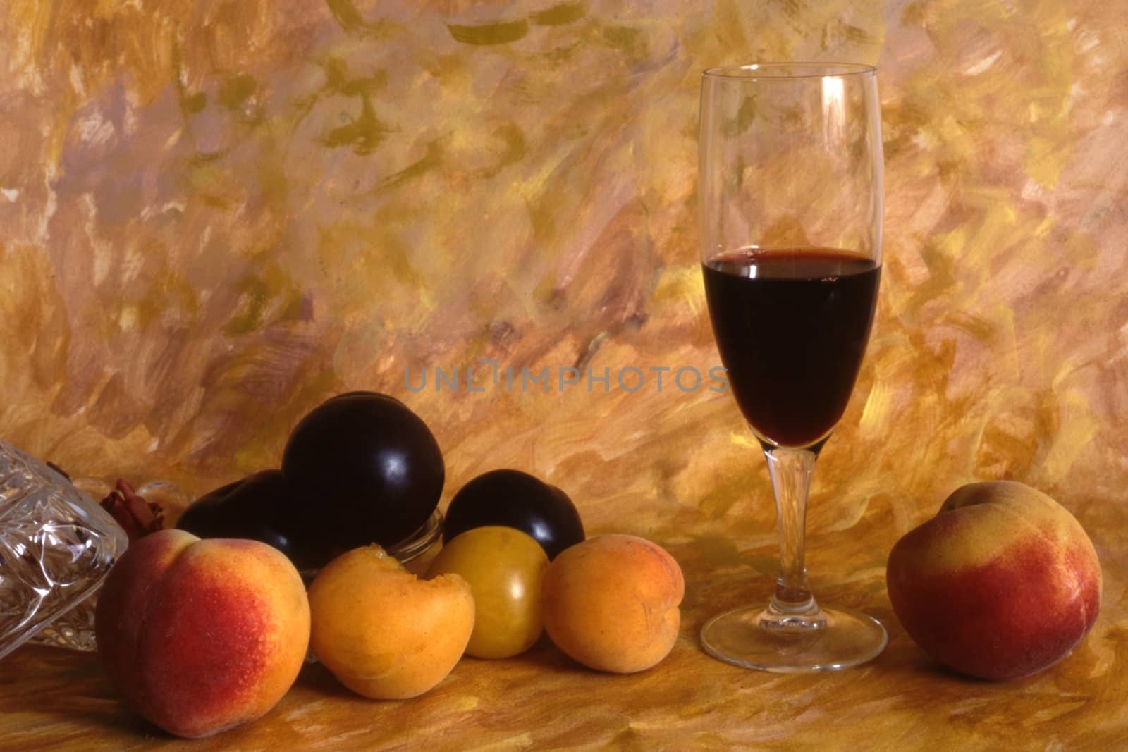 A glass of red wine with fruits on painted background