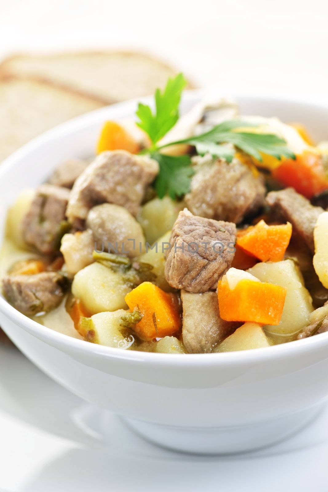 Bowl of hearty beef stew with vegetables served with rye bread