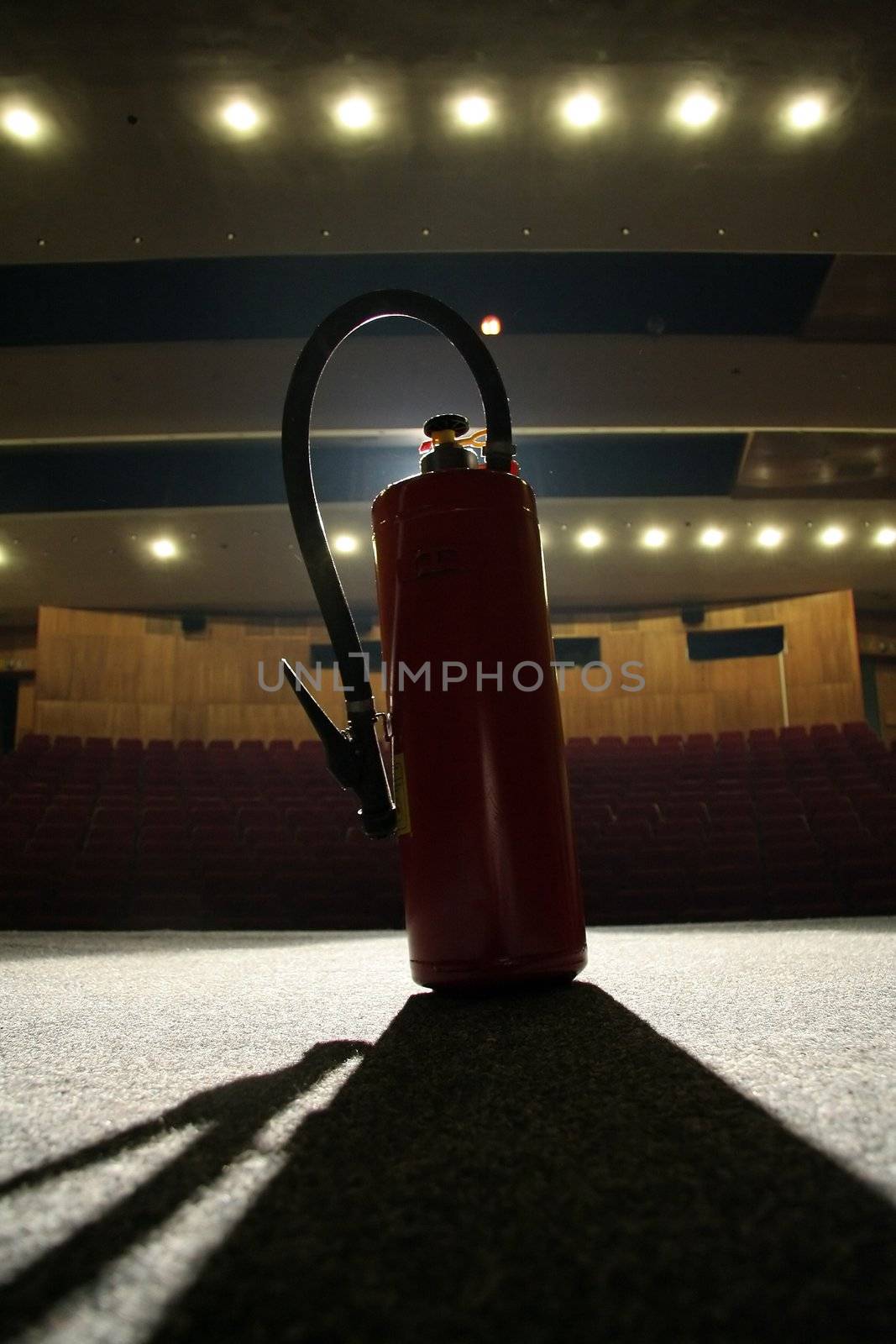 red fire extinguisher on theatre stage, empty seats in background