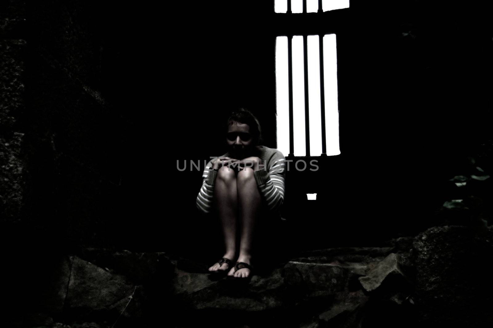 Young woman sitting in a dark dungeon or prison.