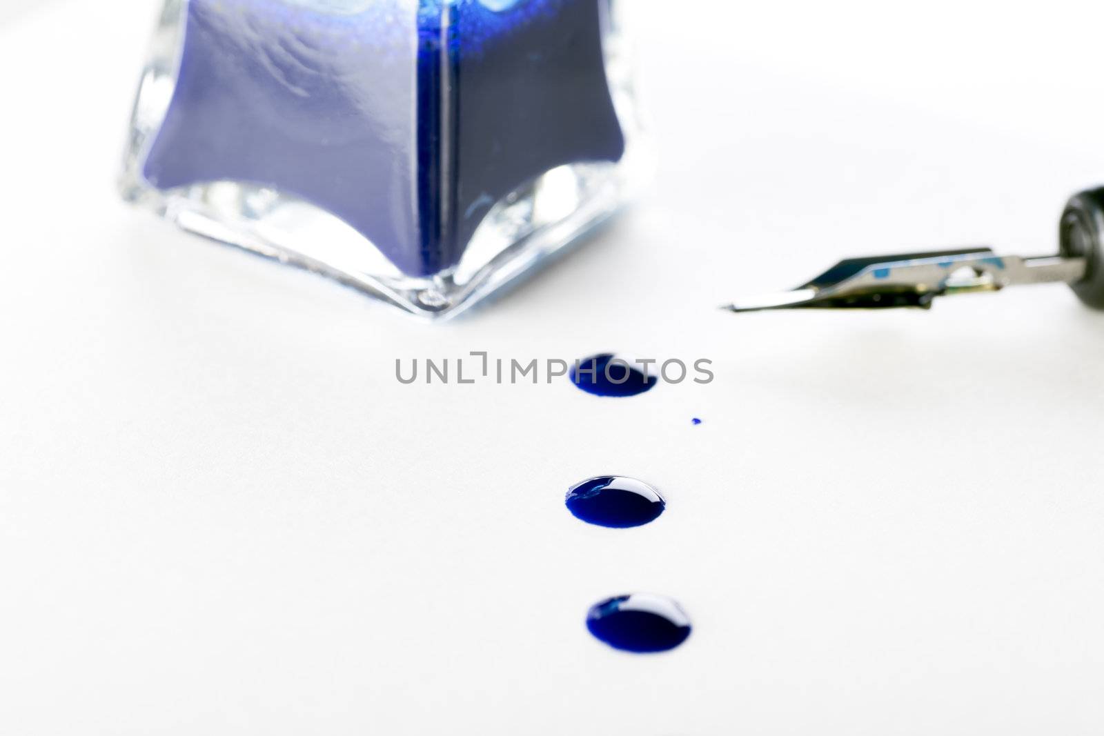 Ink drops on paper with calligraphy pen and bottle of blue ink.