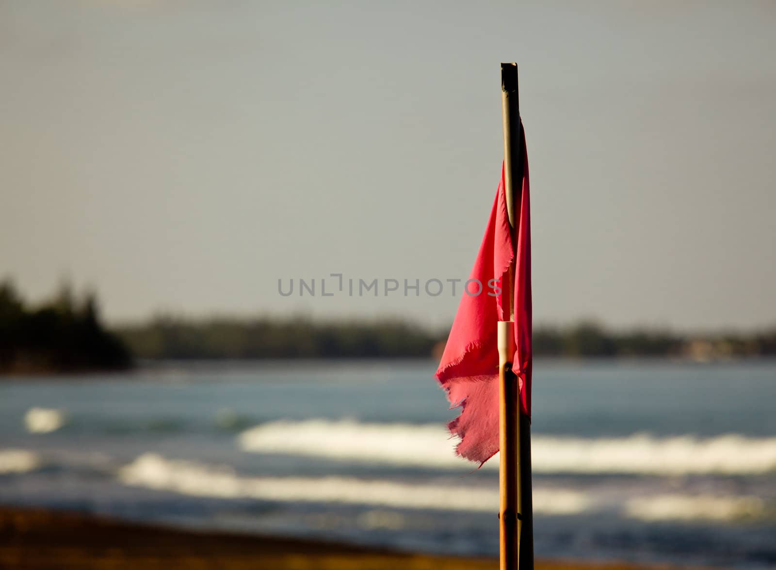 Sun setting lights up red flag signaling danger for swimming in surf