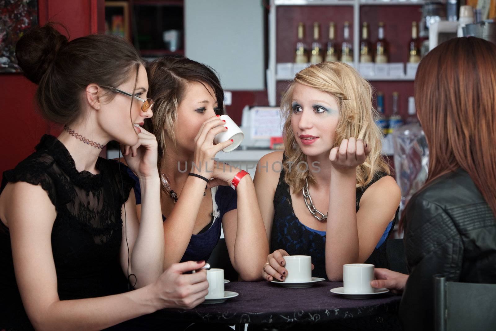 Four young ladies converse over coffee in a cafe