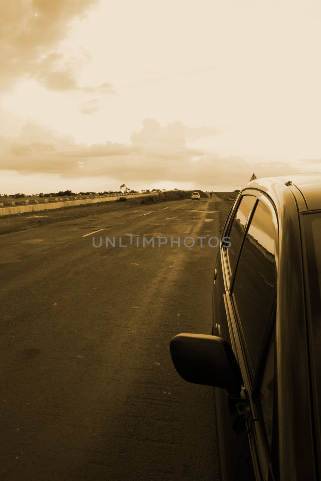 A view of a highway with the reflection of the sky on the windows of a car parked on the side.