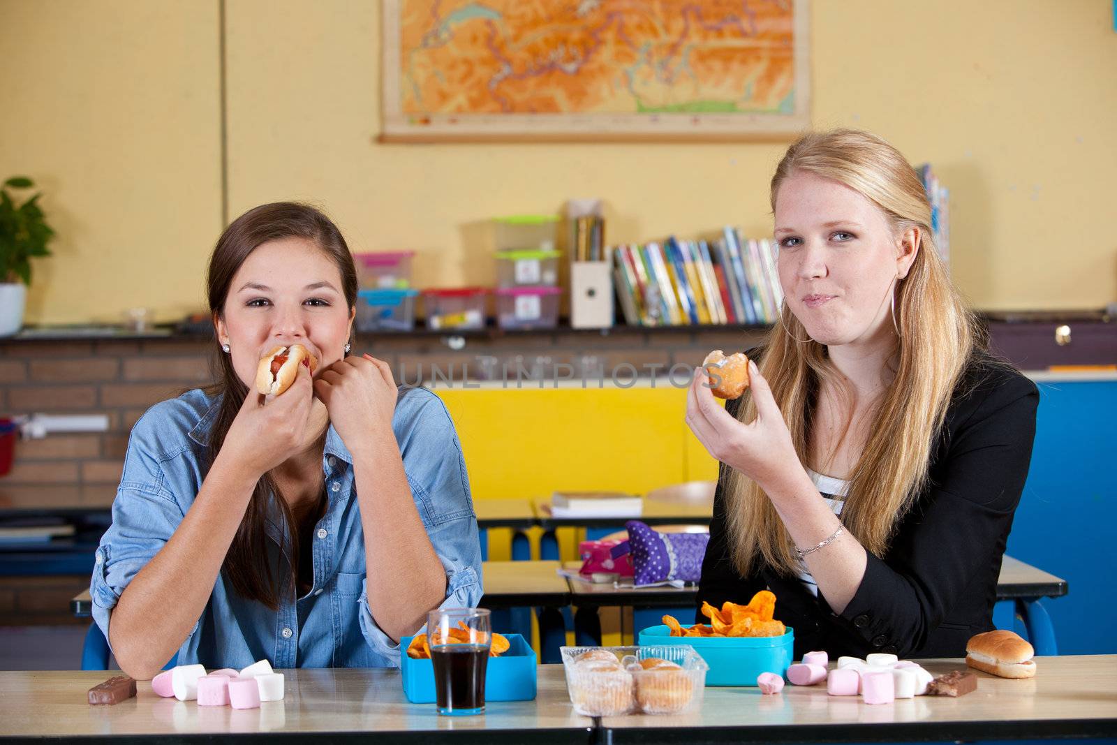Two schoolgirls eating junkfood in classroom