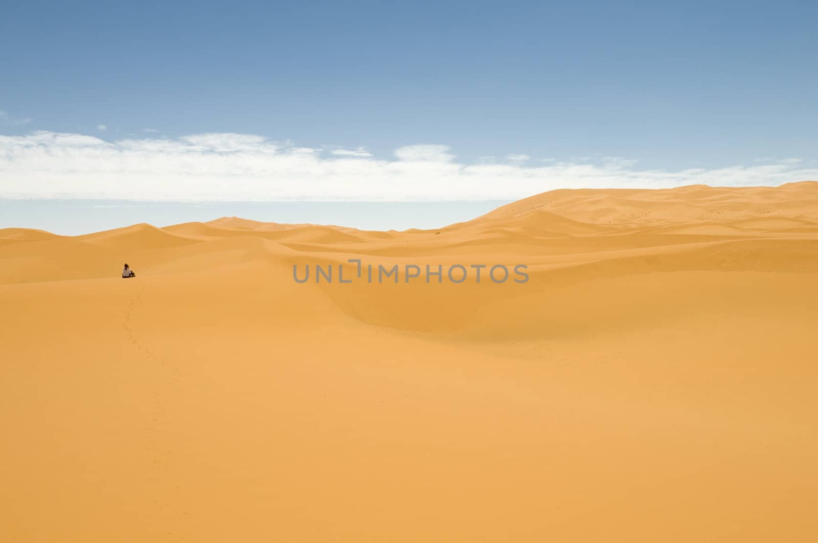 Woman sitting alone into the sand dunes of the Sahara desert. Best of Morocco.