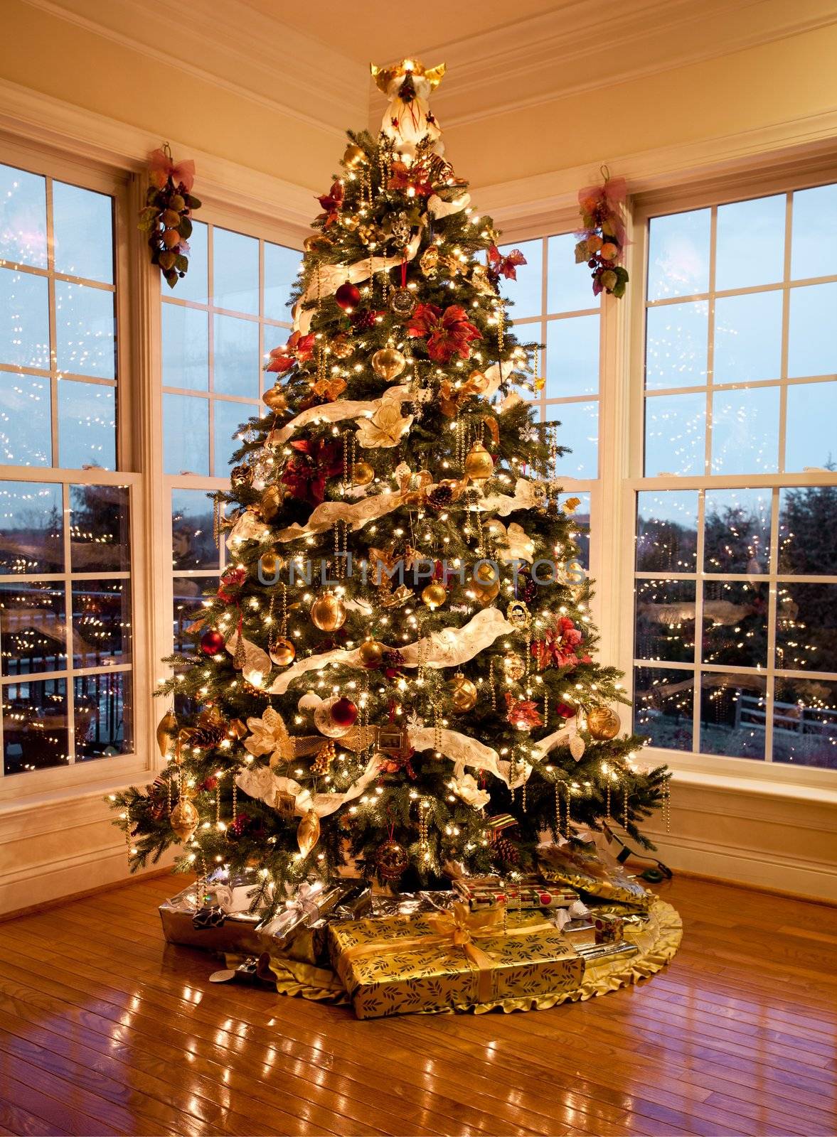 Christmas tree with presents and lights reflecting in windows around the tree in modern home