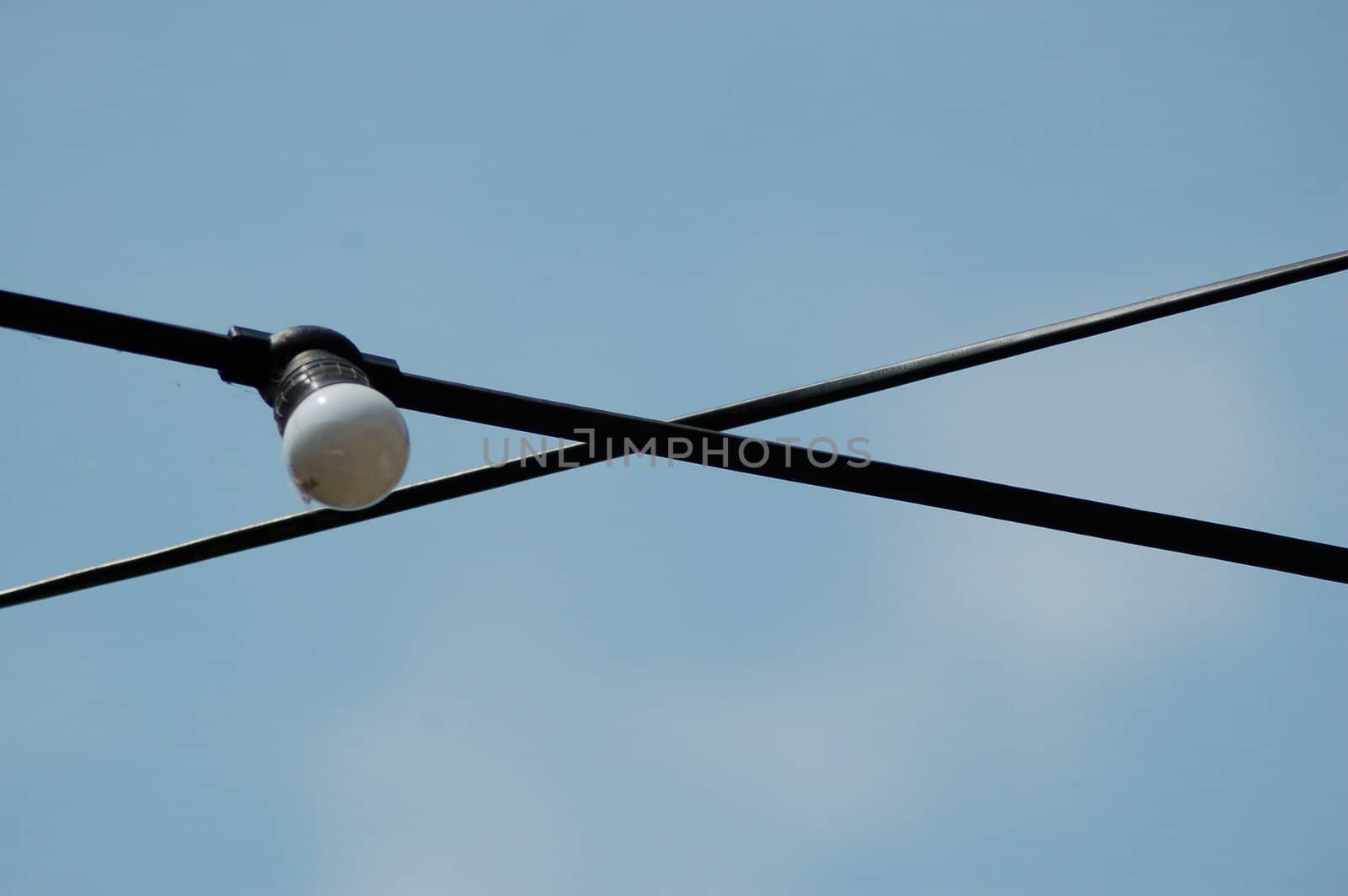 Power cables crossing against a blue sky, featuring one light bulb.