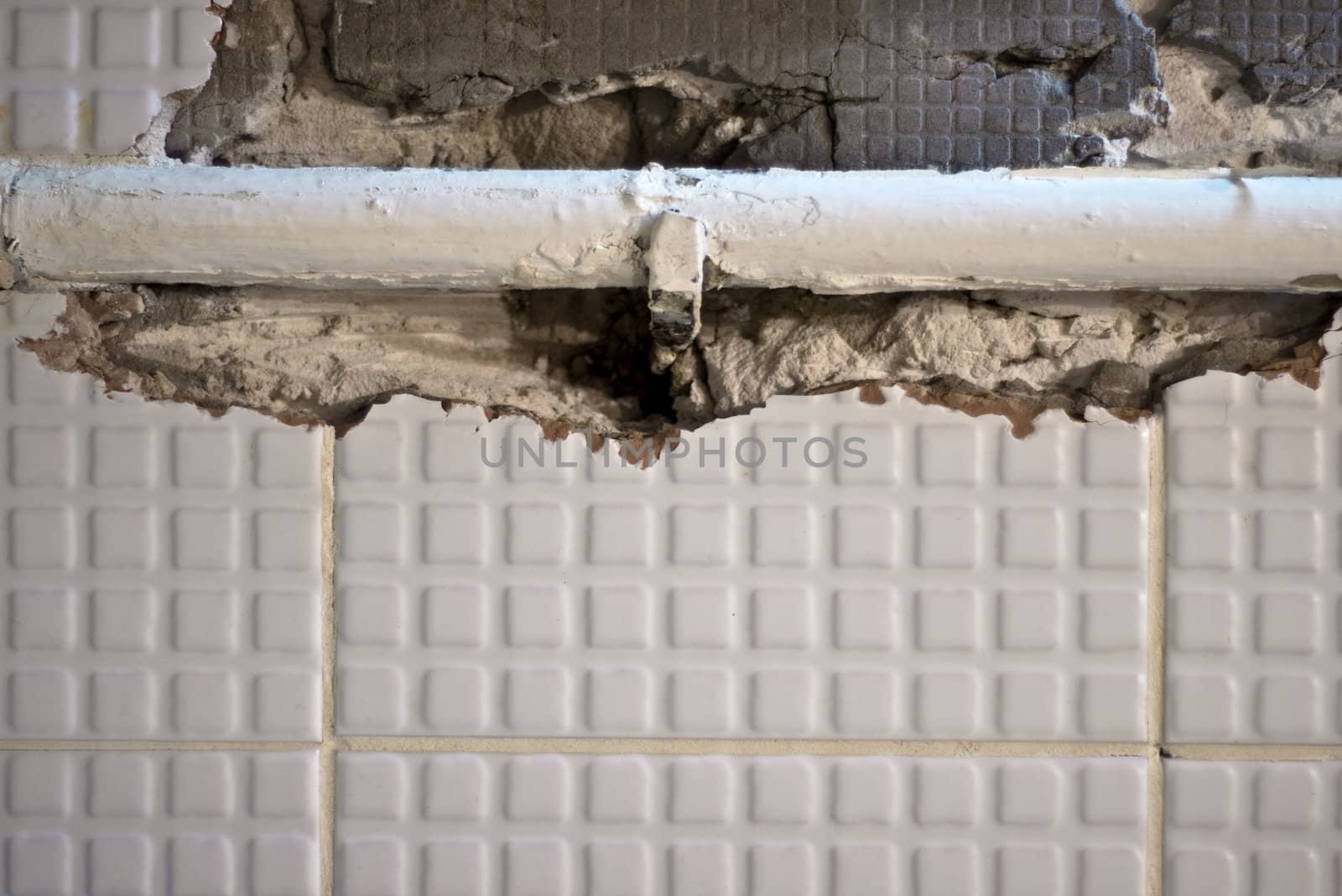 Metal pipe in a ruined wall. Chipped white tiles.