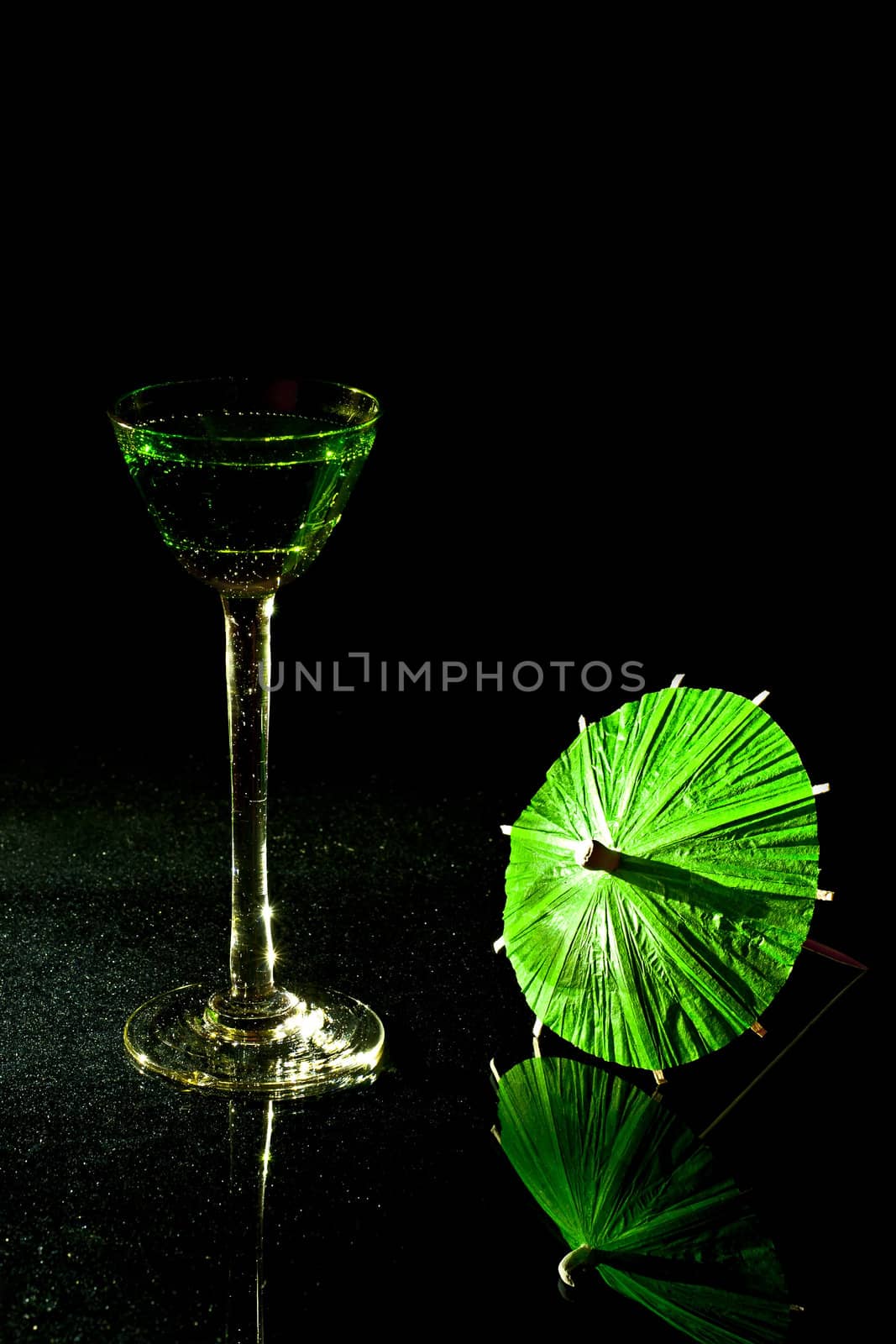 On a black background with green cocktail glass vermouth and a green parasol.
