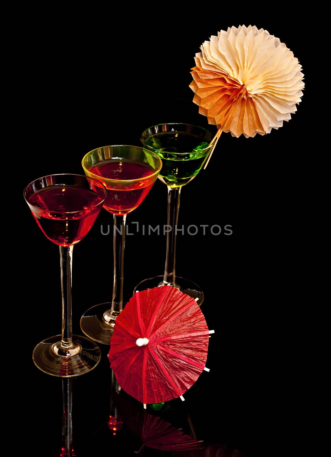 On a black background, three cocktail glasses decorated with parasols.
