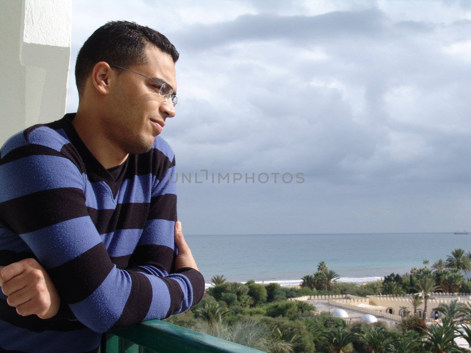 Tunisian man standing on balcony watching tunisian beach resort