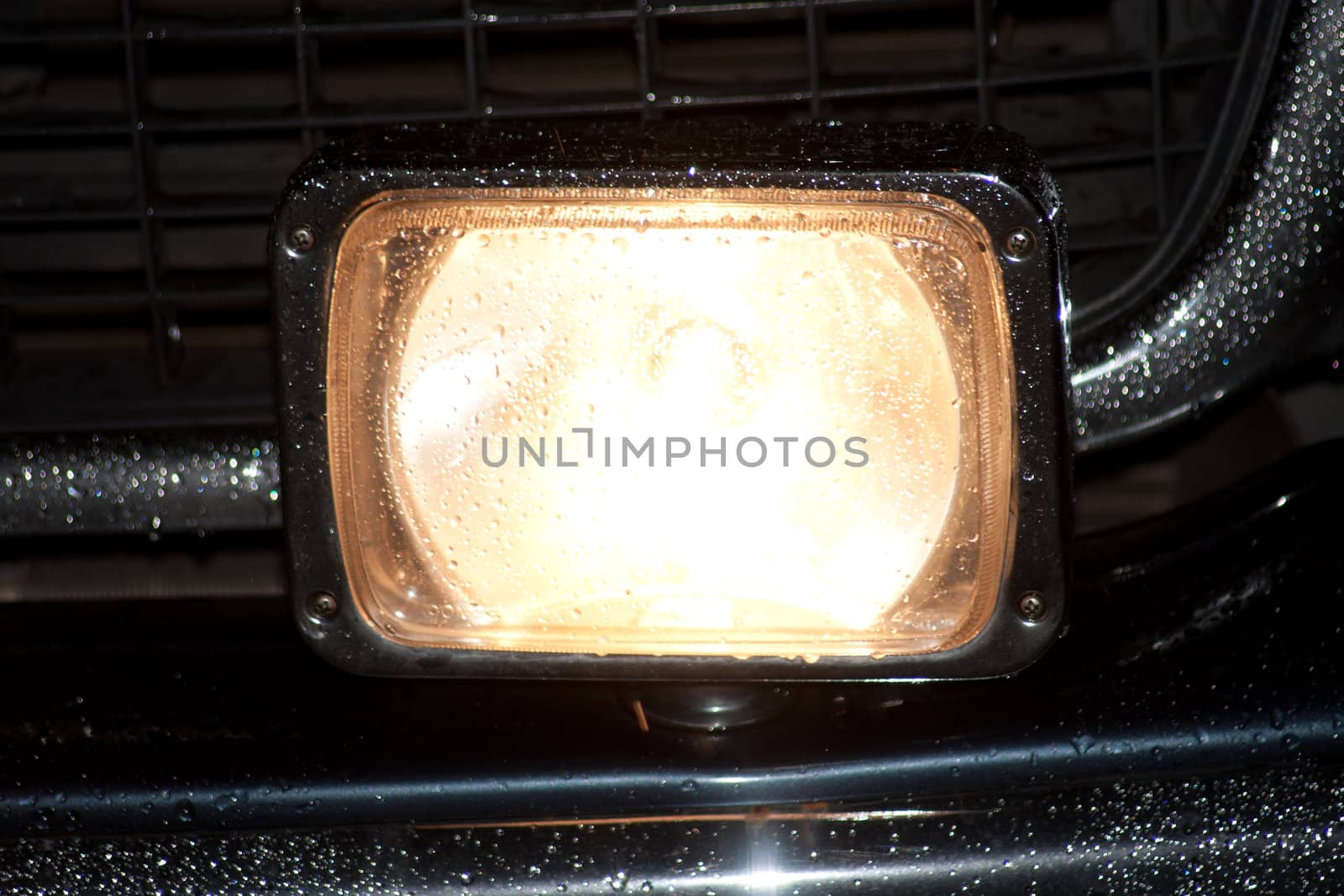 Headlight of an SUV in the rain by night with water