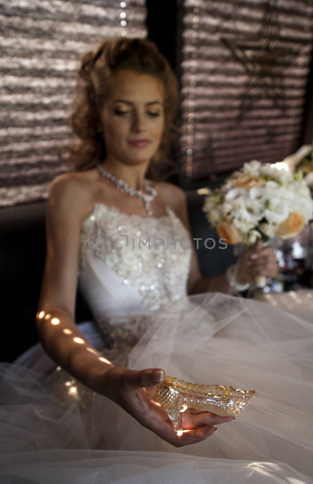 The bride with a crystal shoe. The bride in a wedding dress sits in a limousine holds a crystal shoe.