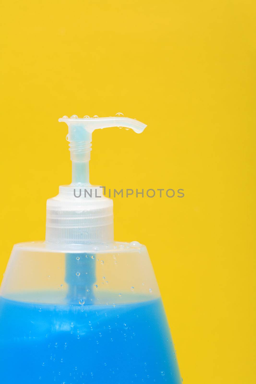Closeup of plastic bottle of blue antibacterial liquid soap on a yellow background
