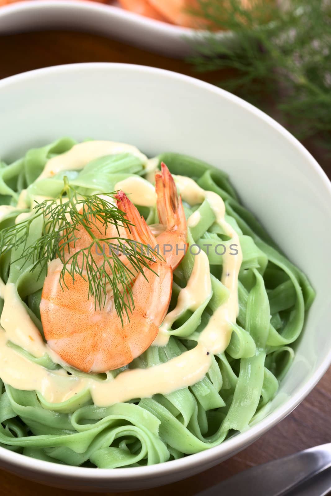 Green tagliatelle (ribbon noodle) with a cream sauce, shrimp and fresh dill served in a bowl (Selective Focus, Focus on the front of the shrimp)