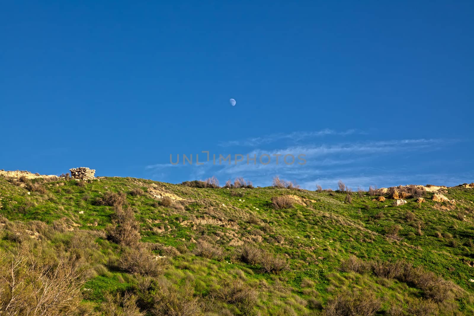 A first quarter moon overlooking the beautiful hillside at Ghajn Tuffieha in Malta.  The deep blue sky adds allure and contrast to the whole picture.