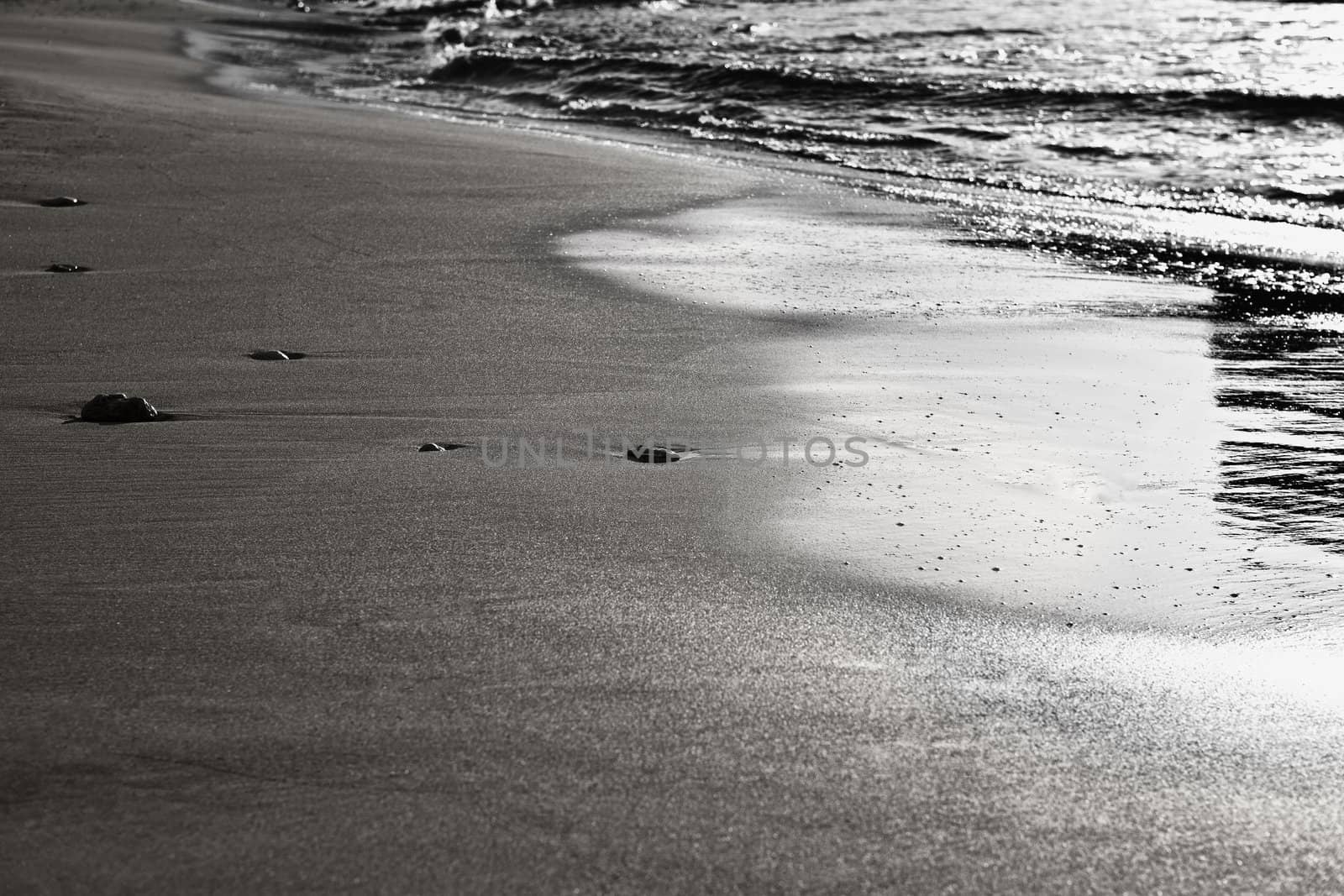 Abstract image showing six pebbles on a sandy beach, seemingly enjoying the gentle ebb and flow of the waves