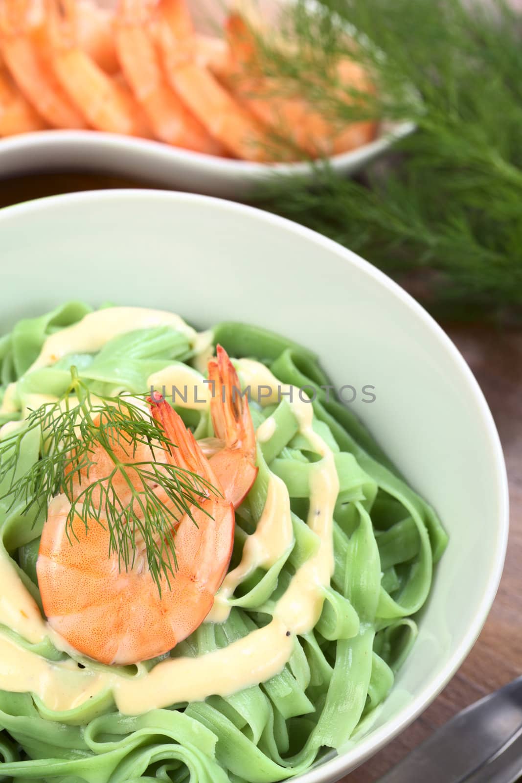 Green tagliatelle (ribbon noodle) with a cream sauce, shrimp and fresh dill served in a bowl (Selective Focus, Focus on the front of the shrimp)