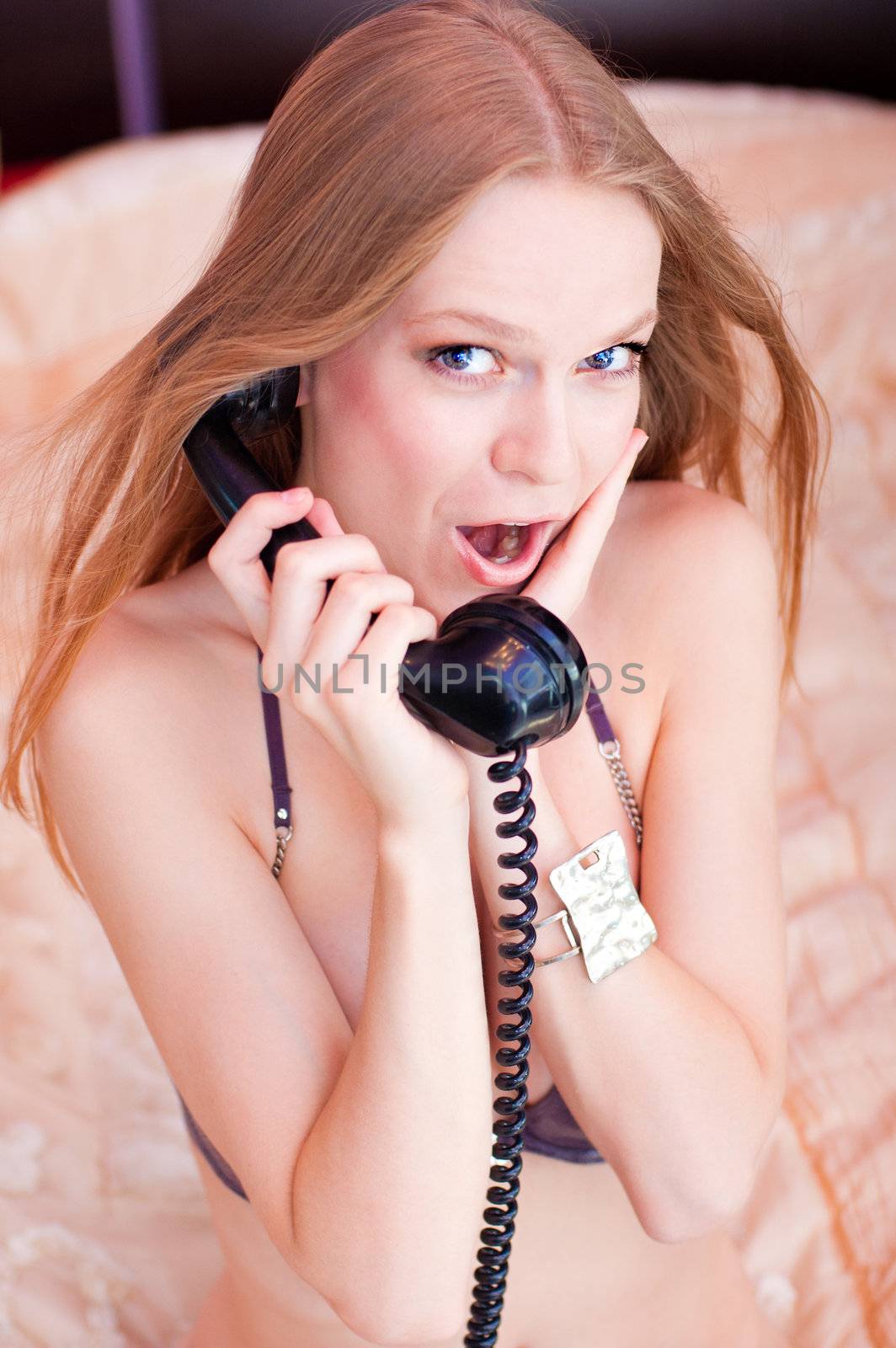 Pretty woman talking by the telephone on a bed in bedroom, dressed in a linen and beads