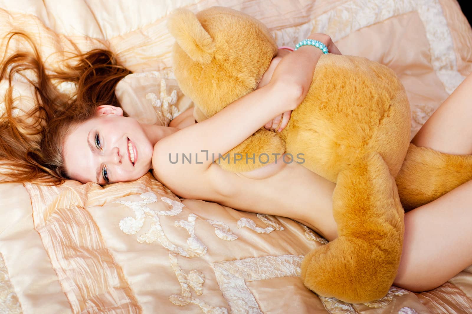 pretty nude woman lies on bed and embreces a teddy bear