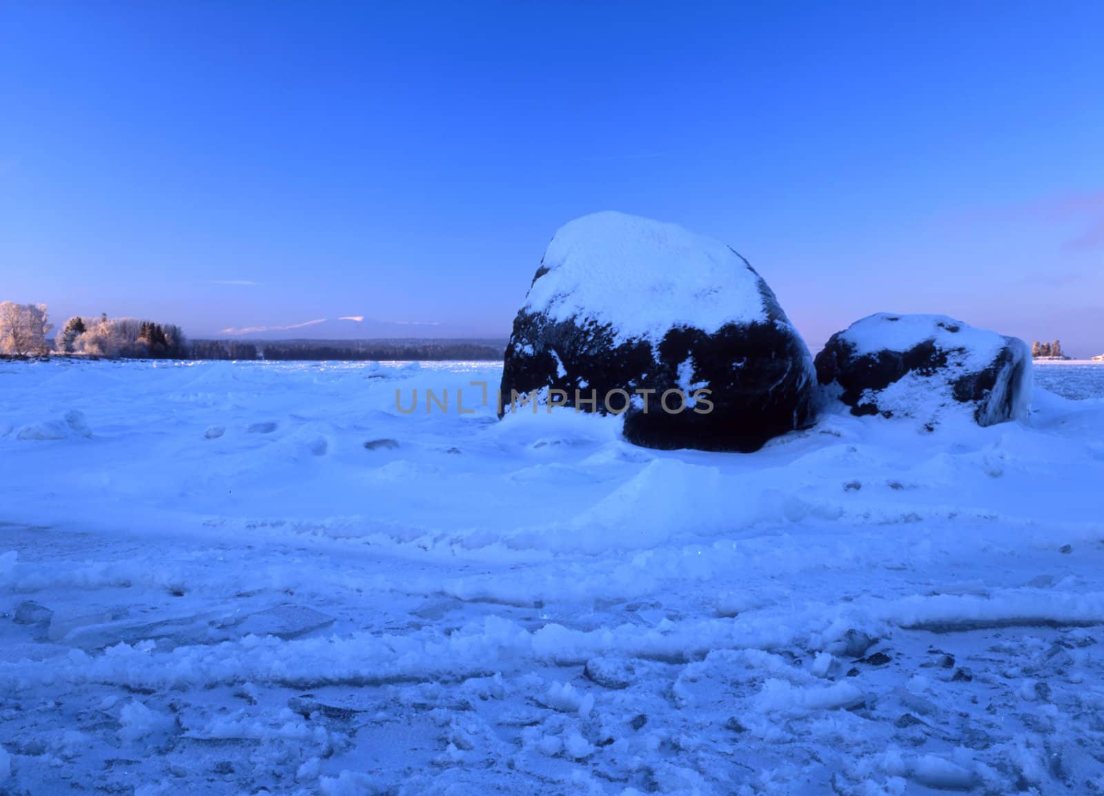 Winter landscape with big snowy stone by the lake
