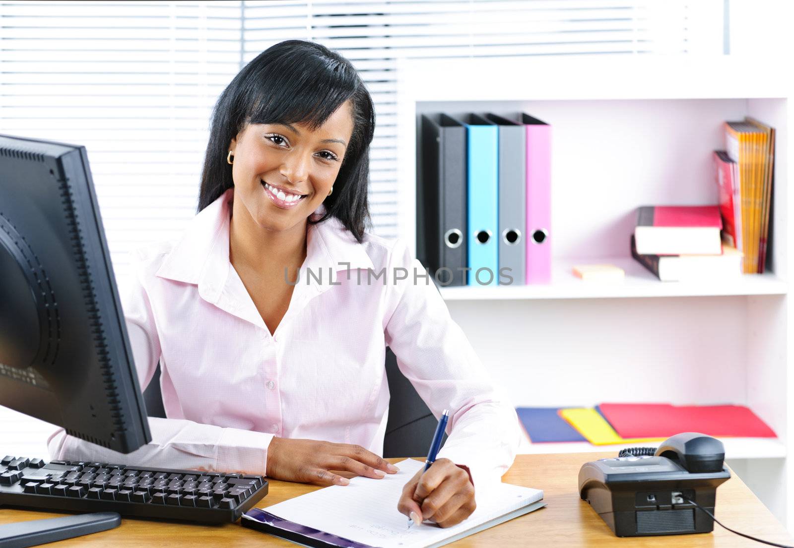 Smiling black businesswoman at desk by elenathewise