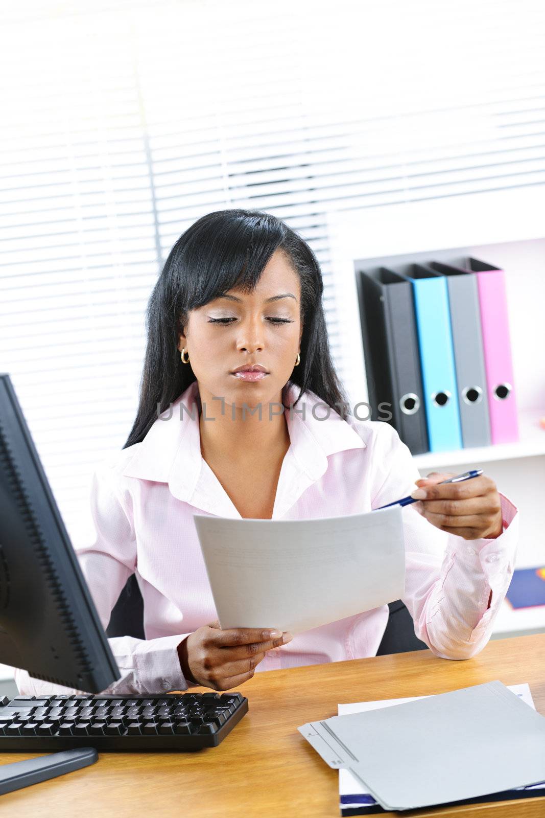 Young black business woman reading document at desk in office